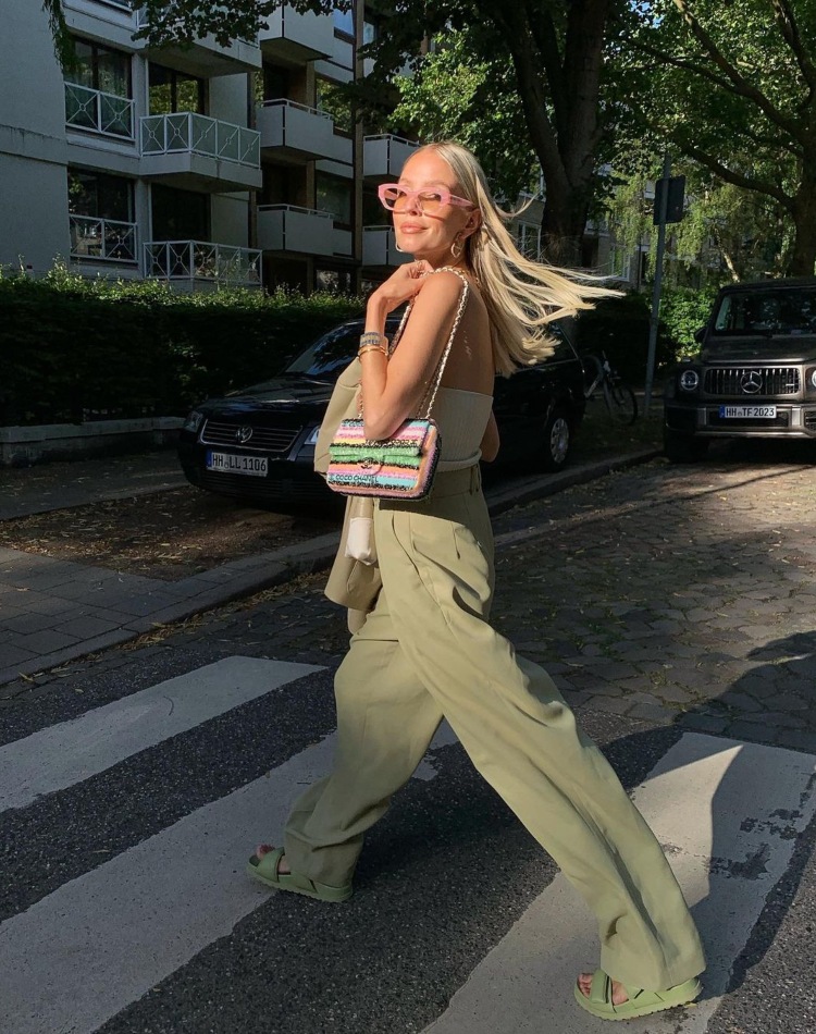 Žena u širokim khaki pantalonama i topu sa šarenom torbom na ramenu